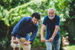 senior father and hipster adult son are happy love and relaxing together at nature outdoor park, mature family of elderly caucasian beard man playing fun with family in retirement leisure time