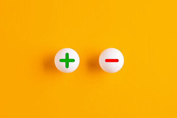 Plus and minus signs on table tennis balls against yellow background.
