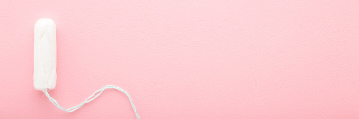 Wall Mural - One new white sanitary tampon on light pink table. Wide banner background. Pastel color. Closeup. Female hygiene. Empty place for text. Top down view.