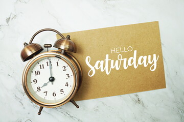 Wall Mural - hello saturday typography text on paper card with alarm clock on marble background