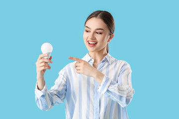 Young businesswoman pointing at light bulb on color background