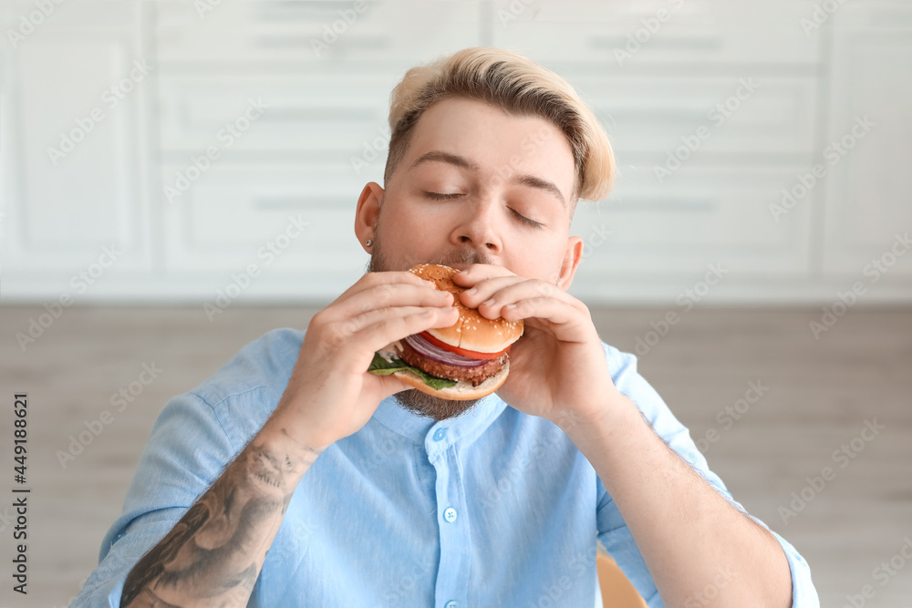 Young man eating vegan burger in kitchen