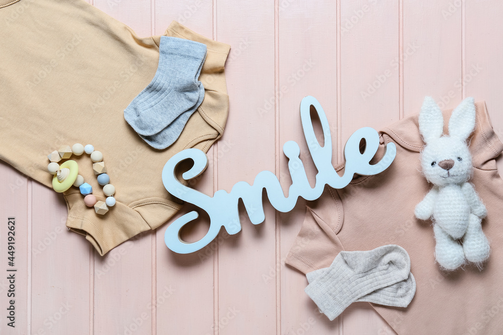 Baby clothes, teether and toy on color wooden background, closeup
