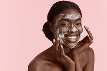 Close Up Portrait Of Beautiful Black Girl Wash Her Face With Cleansing Face Foam. Happy Young Woman Looking At Camera. Concept Of Face Skin Care. Isolated On Pink Background. Studio Shoot