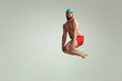Funny cheerful swimmer. Cute red-headed man in red swimming shorts posing isolated on gray studio background. Concept of sport, humor and body positive.