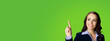 Photo of young brunette woman in black confident suit, showing pointing clicking at mock up copy space free area. Business ad concept. Green color background. Wide horizontal banner image.