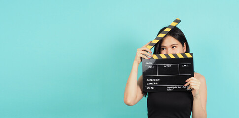 clapper board or movie clapperboard in teenage girl or woman hand with black and yellow color.it use in video production ,film, cinema industry on green or Tiffany Blue background.she wear black dress