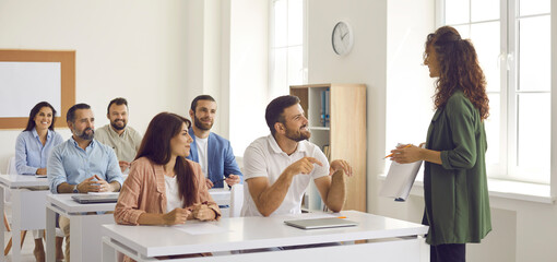 College teacher or business course trainer having discussion with group of people. Happy adult students sitting at tables in classroom, having training class and learning new things. Education concept