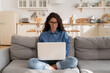 © DimaBerlin - Millennial woman in eyeglasses use laptop computer sitting on couch in living room. Young freelancer worker or student girl shopping online, work remotely or browsing web from home with notebook pc
