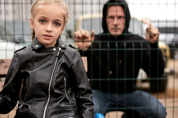 Suspicious adult man spying on kid girl at playground, space for text. Child in danger. focus on caucasian child girl in jacket, on street in city. child abuse, violence concept