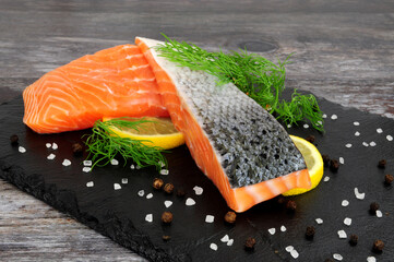 Wall Mural - Two fresh raw salmon fillets with dill herb garnish and lemon slices on a slate serving board