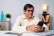 © WESTOCK - Middle aged businessman smiling while using mobile phone at office - concept of using social media, internet, checking mails and communication at workplace
