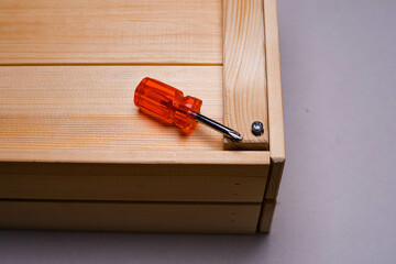 brown wooden box on a white background with a red phillips screwdriver background texture.the screwdriver is lying on a wooden box. the twisted screw is handmade. the box is handmade. wooden box with