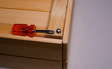 brown wooden box on a white background with a red phillips screwdriver background texture.the screwdriver is lying on a wooden box. the twisted screw is handmade. the box is handmade. wooden box with