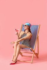 Poster - Beautiful young woman with cocktail sitting on deck chair against color background