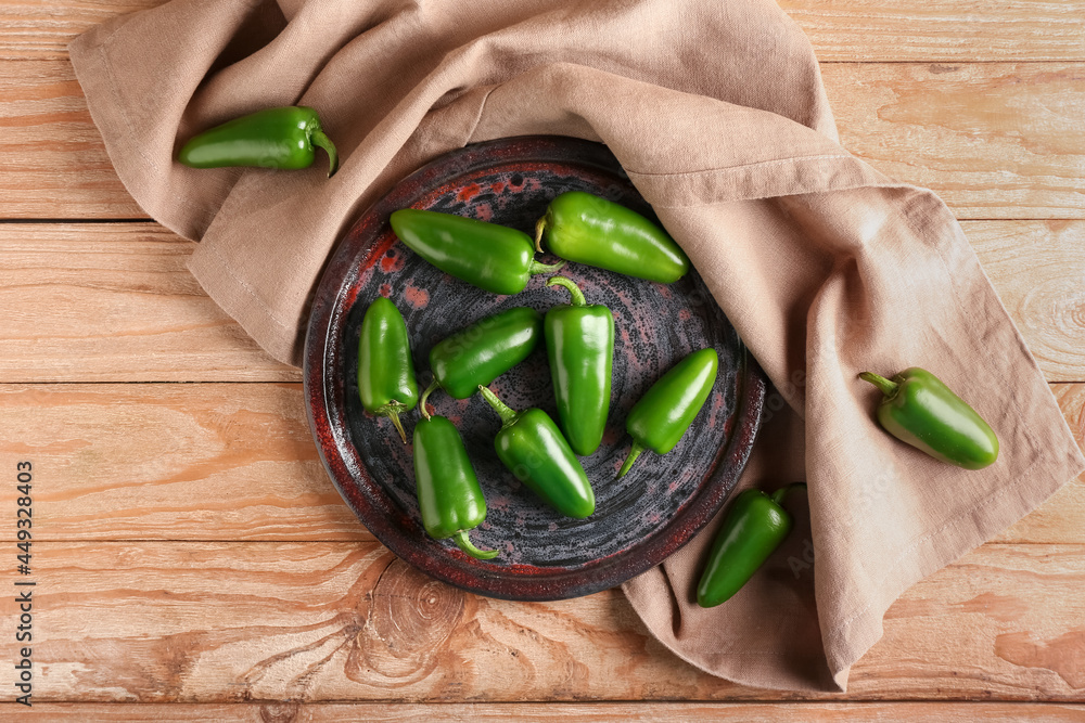 Plate with green jalapeno peppers on wooden background