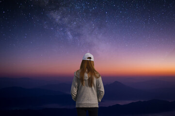 Wall Mural - Young female wearing grey sweater looking beautiful view of night sky and star and milky way alone on top of the mountain. She enjoyed traveling and was successful when he reached the summit.