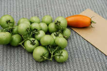 Close Up Of Heap Of Green Tomatoes, Orange Pepper And Beige Envelope On A Gray Decorated Surface