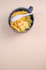 Sticker - Vertical shot of corn flakes on a cup with plastic spoon isolated on brown background