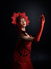 Wall Mural - Full length  portrait of beautiful young asian woman wearing red corset, long opera gloves and ornate gothic queen crown. Graceful posing isolated on a dark studio background.