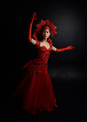 Wall Mural - Full length  portrait of beautiful young asian woman wearing red corset, long opera gloves and ornate gothic queen crown. Graceful posing isolated on a dark studio background.