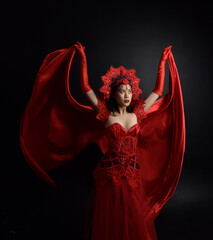 Wall Mural - Full length  portrait of beautiful young asian woman wearing red corset, long opera gloves and ornate gothic queen crown. Graceful posing isolated on a dark studio background.