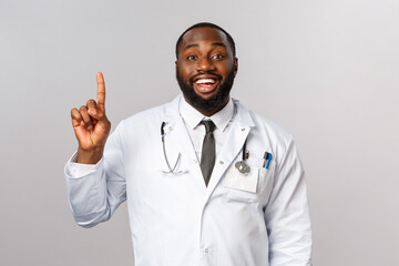 Portrait of cheerful african-american male doctor explain one simple task for patient stay healthy, not getting covid19, make daily check-up in hospical, smiling and showing number one, index finger