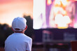 A boy in a cap watching a movie in the open air
