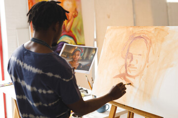 African american male painter at work painting portrait on canvas in art studio