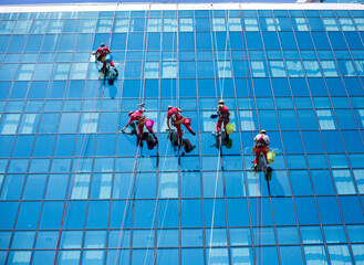 Five brave men hanging on the rope and washing windows on the glass covered building