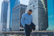 © Alexander Image - A young black businessman is standing in a business district, looking down and into deeply thinking..