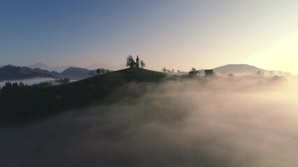 Wall Mural - Aerial landscape of mountain hills covered in fog and Saint Thomas church, Slovenia on sunset