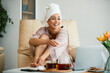 Happy beautiful woman uses laptop while having pedicure at home.