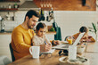 © Drazen - Little girl sits on father's lap while he is writing notes and working on laptop at home.