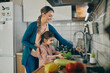 © Drazen - Happy mother and daughter wash vegetables while preparing food in the kitchen.