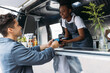 Young man with credit card paying to a saleswoman at a food truck. Female entrepreneur in apron receiving payment from a customer.