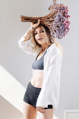 Portrait of a beautiful young girl in white shirt, black top and shorts, holding a big bouquet of dried flowers over gray background splashed by lines of light