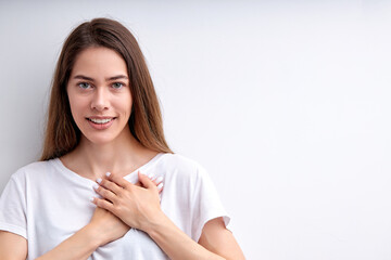 Adorable happy woman expressing gratitude, holding hands on chest, thankful for everything, looking at camera having nice smile, casually dressed. isolated on white studio background, copy space