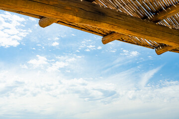 Wall Mural - (Selective focus) Stunning view of a blue sky with some clouds during a sunny day and a wooden roof in the foreground. Natural background with copy space.