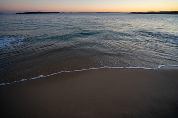 Wall Mural - View of lapping waves on sand at sunset