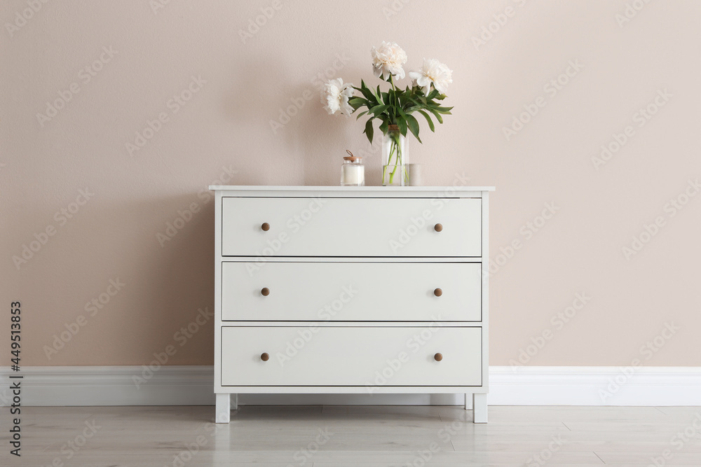 White chest of drawers with bouquet and candle near beige wall - obrazy, fototapety, plakaty 