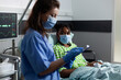 © DC Studio - Nurse examining patient healthcare and illness immunity sitting in hospital ward. Caucasian woman checking treatment progress on young african american adult laying in bed at medical clinic