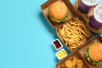 Flat lay composition with delicious fast food menu on light blue background. Space for text