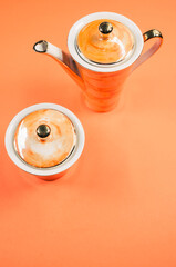 Sticker - Close up of an orange covered teapot and a covered cup on an orange isolated background, free space