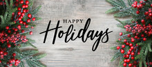 Happy Holidays Text With Holiday Evergreen Branches And Red Berries Frame On Sides Over Rustic Wooden Background