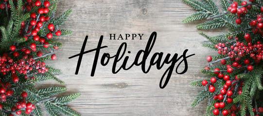 happy holidays text with holiday evergreen branches and red berries frame on sides over rustic woode