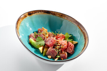 Wall Mural - Tuna and avocado salad bowl. Blue salad bowl isolated on white background. Salad garnished with micro greens and sesame, chopped tuna, sliced avocado and parsley green leaf. Raw tuna with spicy sauce.