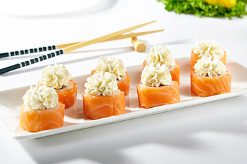 Canvas Print - Philadelphia Sushi Roll made with Smoked Salmon. Maki sushi topped with cream cheese. White plate with wooden chopstick on white table.