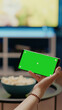 Person holding modern phone with horizontal green screen for chroma key and copy space with isolated background. Young woman sitting at home with equipment and mockup layout for template