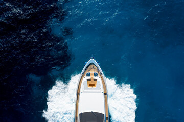 Wall Mural - View from above, stunning aerial view of a luxury yacht cruising on a blue water with waves crashing on the bow of the boat. Costa Smeralda, Sardinia, Italy.
